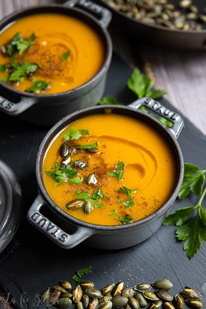 Soupe patates douces, carottes et gingembre dans un bol, garnie d'herbes fraîches