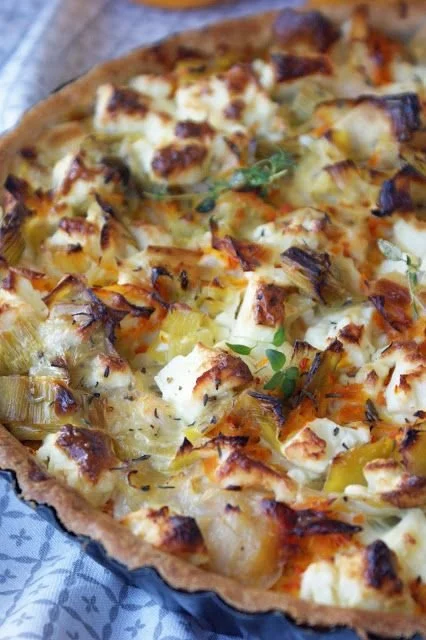 Tarte potimarron poireau et féta sur une assiette avec une garniture dorée